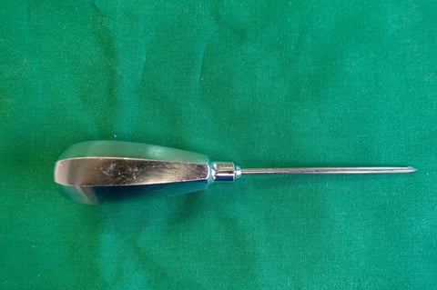 on a green surgical drape lies an awl for an operation