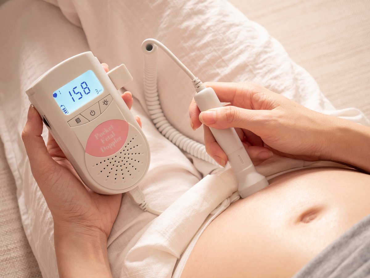 asian woman using pocket fetal doppler to monitor baby heart beat. expectant mother happy and smile when examine belly.