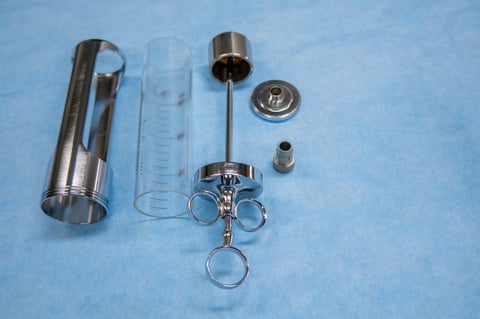 A disassembled urological bladder syringe lies on a blue OP base