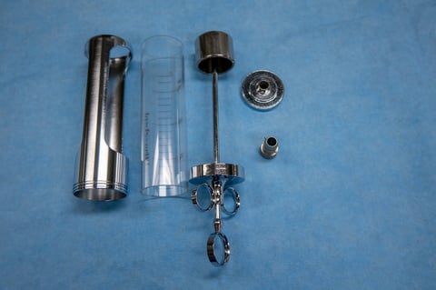 A disassembled urological bladder syringe lies on a blue OP base