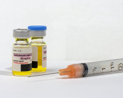 Two vials of injectable generic Methotrexate isotonic liquid and a hypodermic syringe on a white surface.