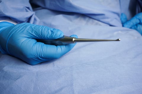 Doctor wearing blue medical gloves holding bone curette.