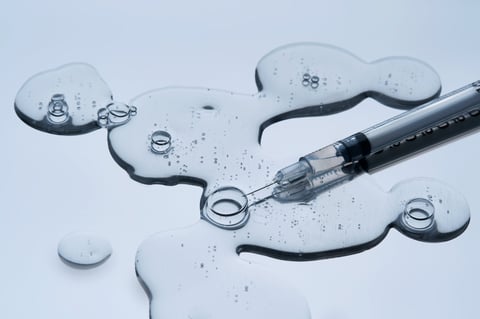 The texture of a cosmetic preparation and a syringe for injection on a blue background