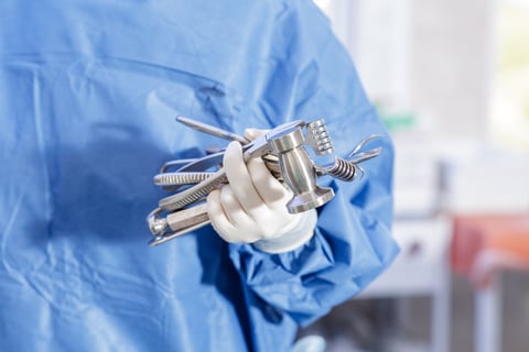 Close view of a gloved hand holding stainless surgical tools in a sterile OR