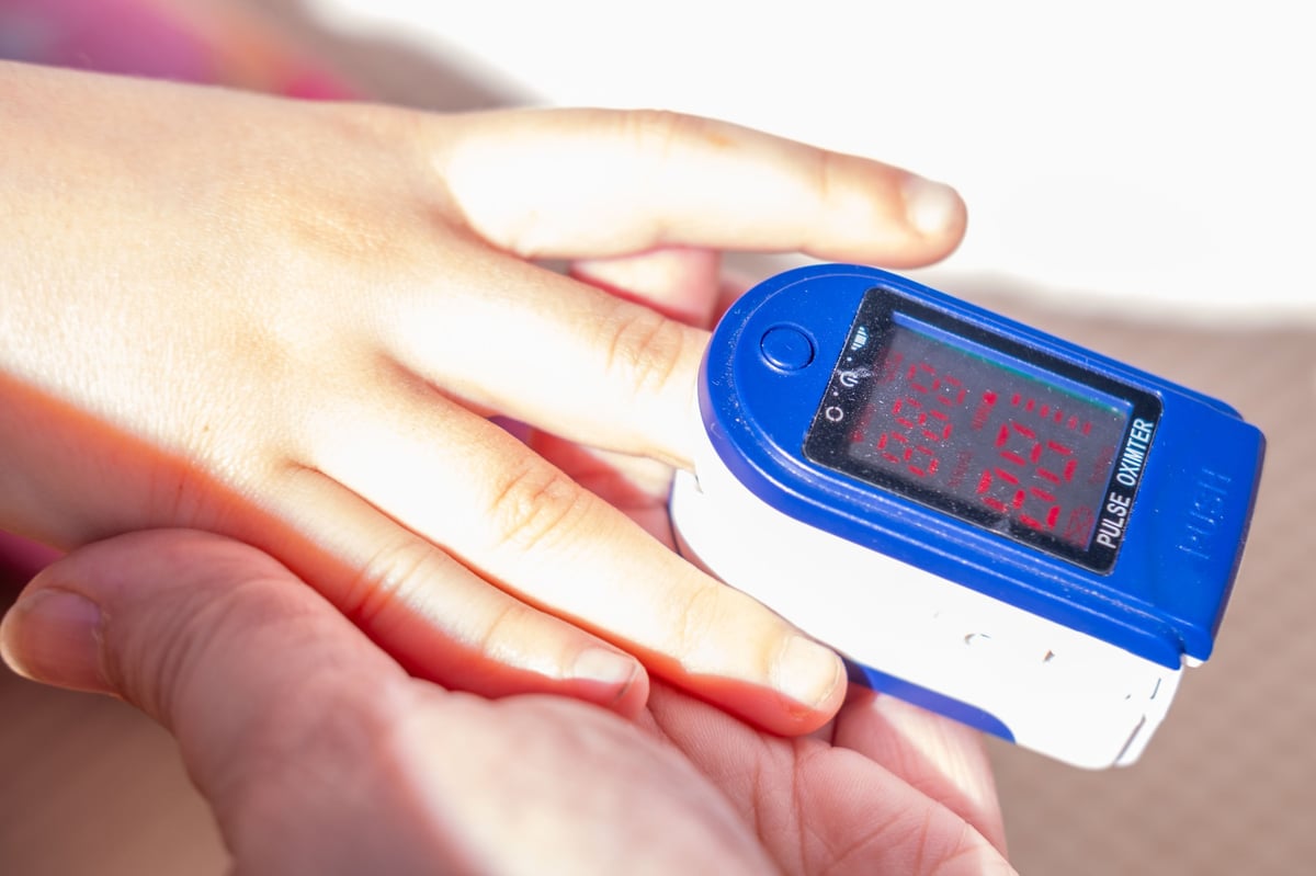Close up of a blue pulse oximeter on a child's finger, held gently by an adult's hand, monitoring oxygen saturation and heart rate, medical checkup, Respiratory health care, pediatric diagnostic tool