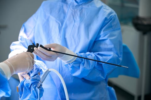 Two surgeons in surgical gowns and gloves focus on a laparoscopic procedure in a sterile hospital operating room. The atmosphere is professional and clinical during daytime.