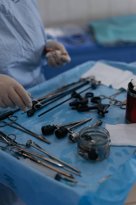 Close-up of various laparoscopic surgical tools and metal instruments arranged on sterile blue medical table. Surgeon hands in gloves preparing equipment for minimally invasive procedure in clinic.