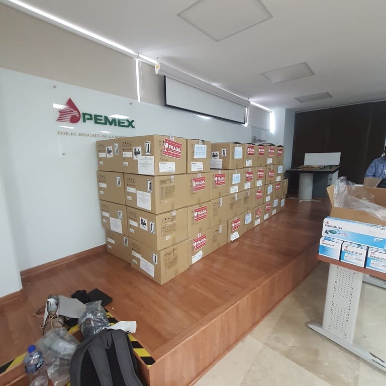 Pemex office interior with cardboard boxes stacked on wooden platform and company logo on white wall