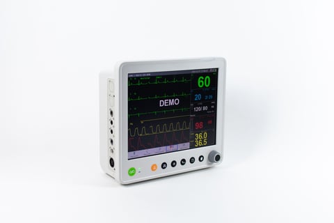 White medical monitor displaying heart rate and vital signs with waveforms on screen and control buttons below