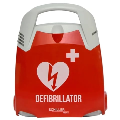 Red and white defibrillator device with heart and lightning bolt logo, labeled DEFIBRILLATOR SCHILLER