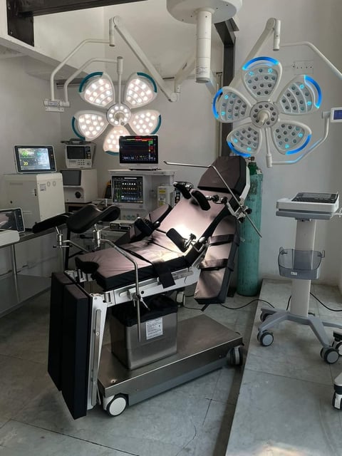 Modern surgical operating room with overhead LED lights, monitoring equipment, and patient examination bed surrounded by medical instruments and mobile stands