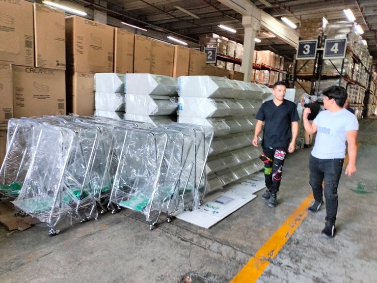 Two workers walking past pallets of wrapped mattresses and boxed inventory in a warehouse with yellow floor line