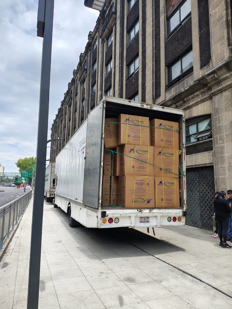 White delivery truck with open rear doors loaded with stacked cardboard boxes parked on a city street next to buildings
