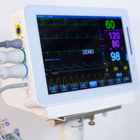 Medical monitor displaying vital signs including heart rate, blood pressure, oxygen saturation, and waveforms with multiple sensor cables attached