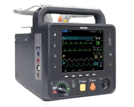 Philips portable defibrillator monitor displaying heart rhythm waveforms and vital signs on screen with control buttons and paddles