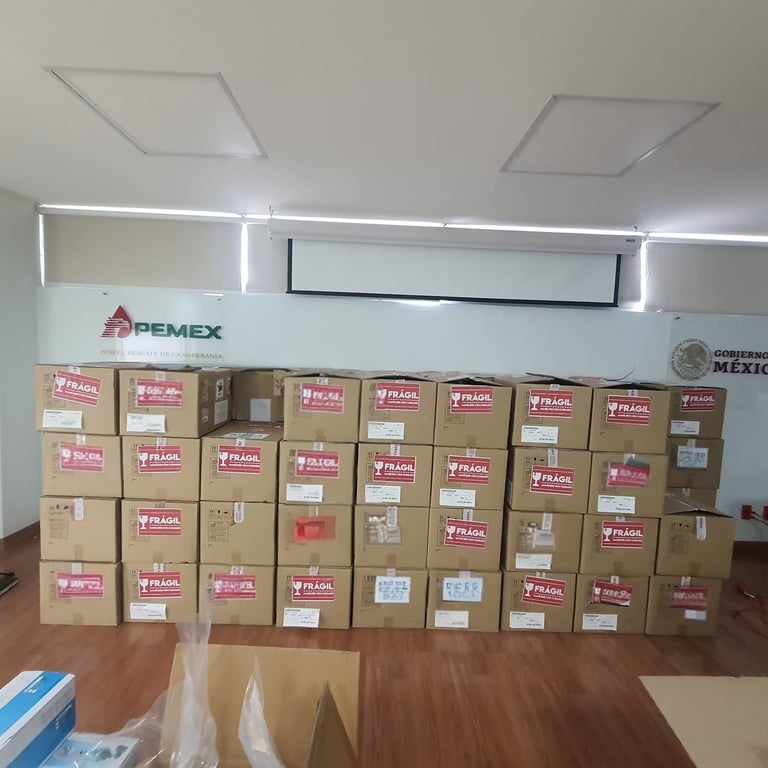 Wall of stacked cardboard boxes with PEMEX branding and pink labels in an indoor storage or warehouse space with wooden floor and fluorescent lighting