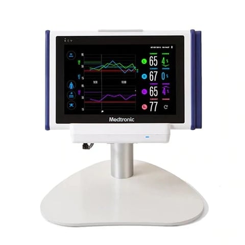 Medtronic patient monitor displaying vital signs with multiple colored waveforms and numerical readings on a white pedestal base