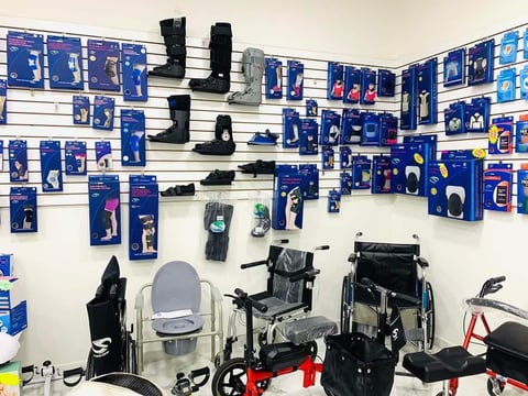 Retail display of mobility aids and assistive devices including wheelchairs, walkers, and boots with blue product boxes on wall shelves