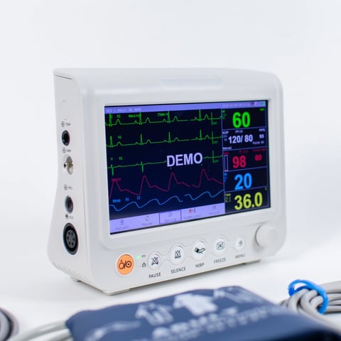 Portable medical patient monitor displaying vital signs including heart rate, blood pressure, and temperature with waveform tracings on screen